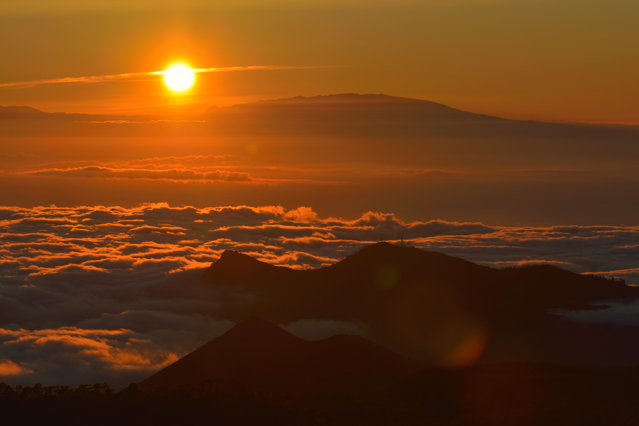 Sunset over mountains with clouds below, creating a vibrant orange sky.