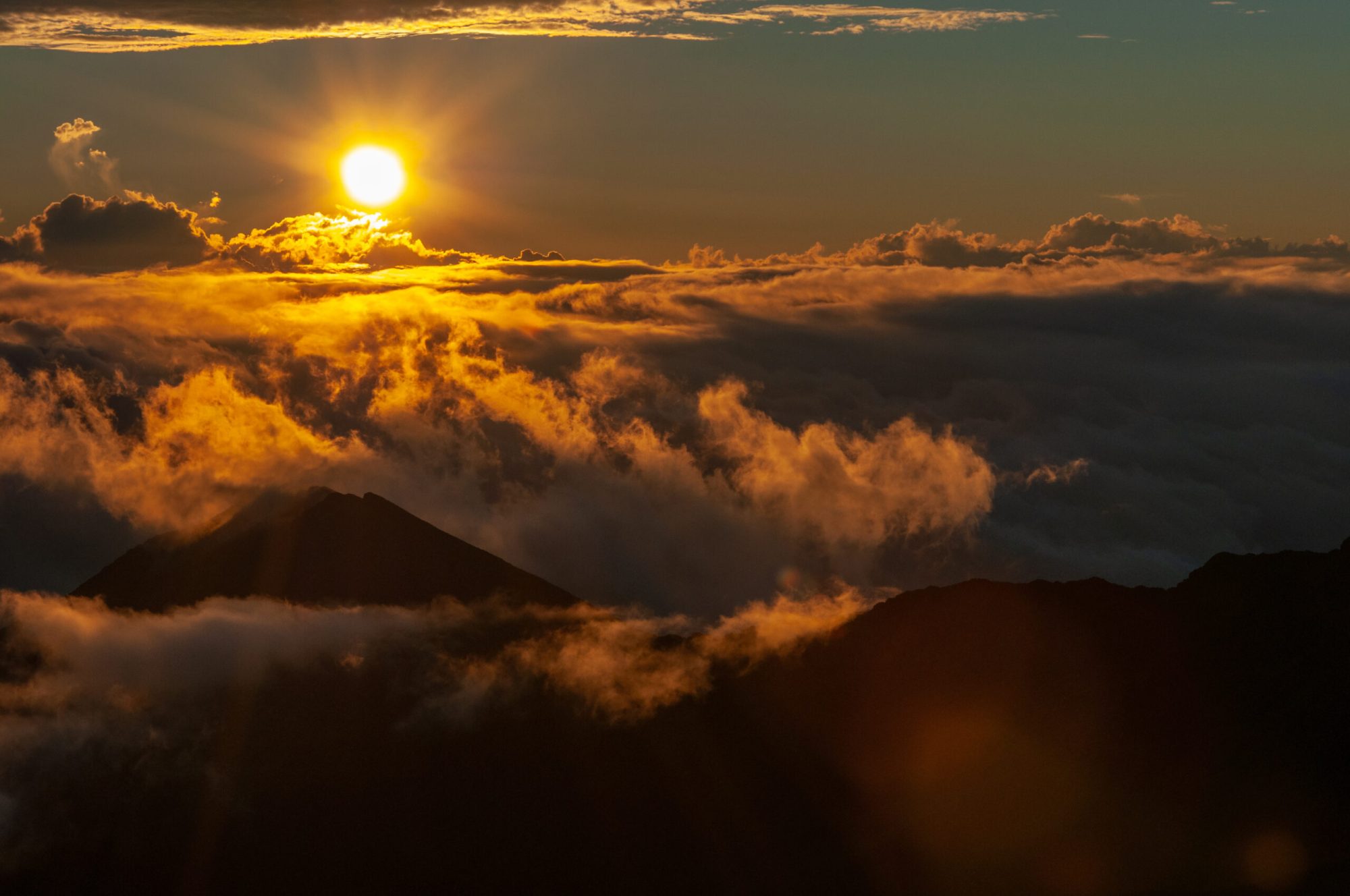 Sunset over mountain with clouds and vibrant orange sky.