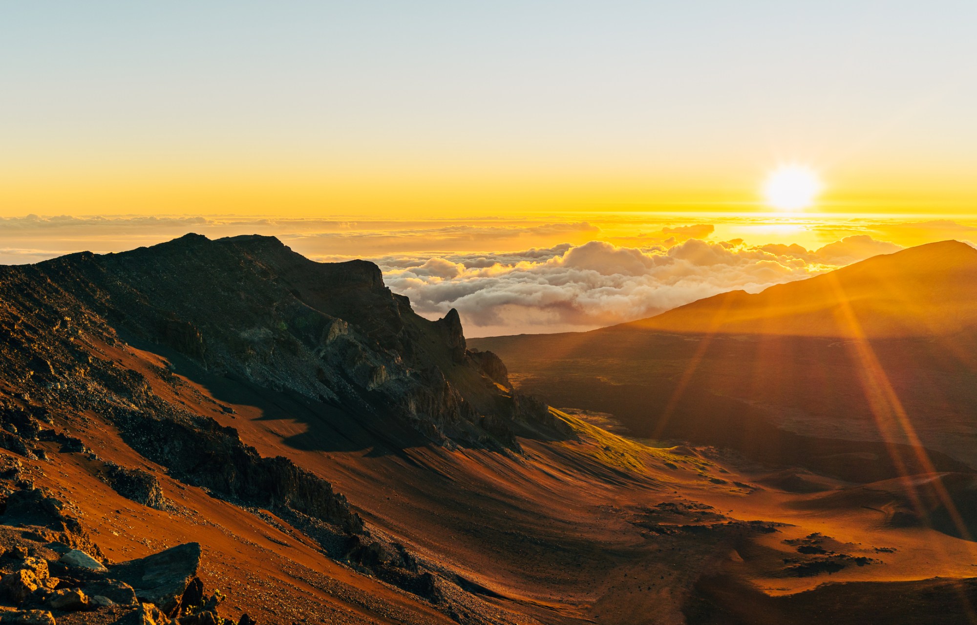 Sunrise over mountain landscape with clouds and sunlight beams.