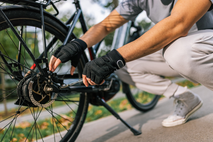 Person wearing gloves kneeling beside a bicycle, adjusting the rear wheel.