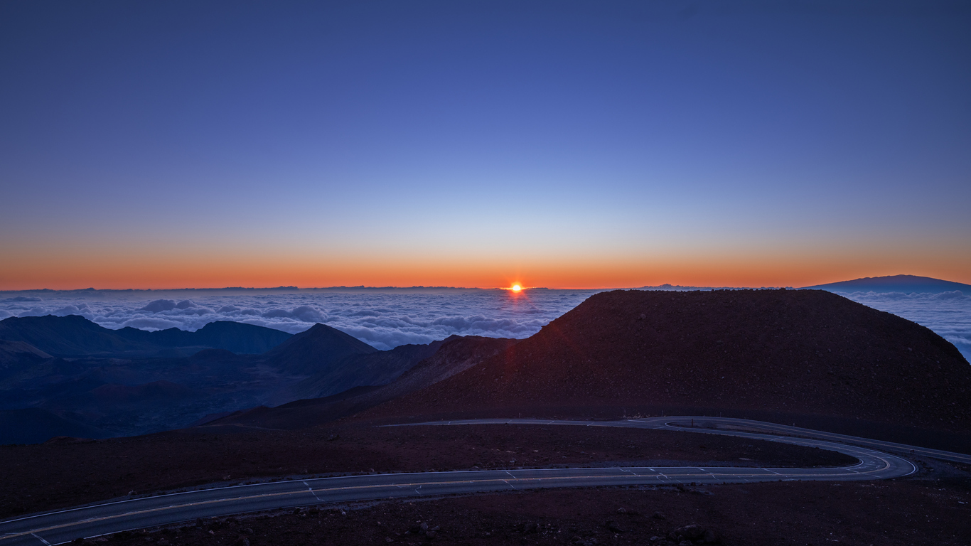 Sunrise over a mountain landscape with a winding road and cloud-filled sky.