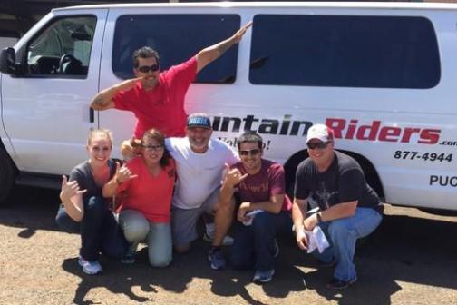 Group of six people posing in front of a white 'Mountain Riders' van.