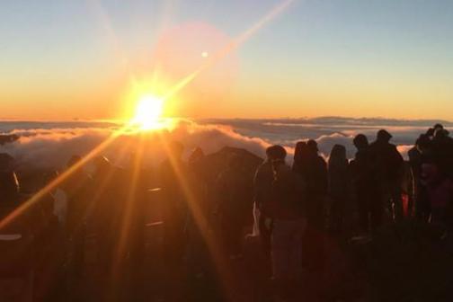 Silhouetted crowd watching sunrise over clouds and mountains.