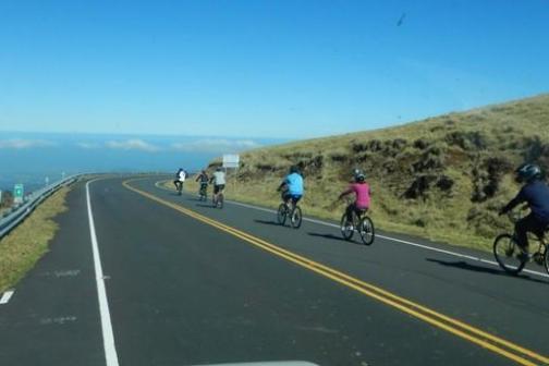 Group of cyclists on a road with grassy hills and blue sky in the background.