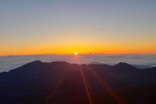 Sunrise above mountains with a clear sky and clouds at horizon.
