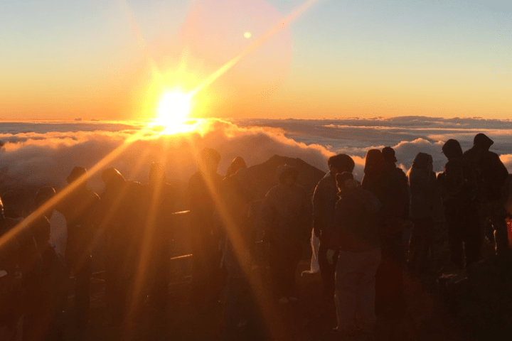 Silhouettes of people watching a sunrise above the clouds on a mountaintop.