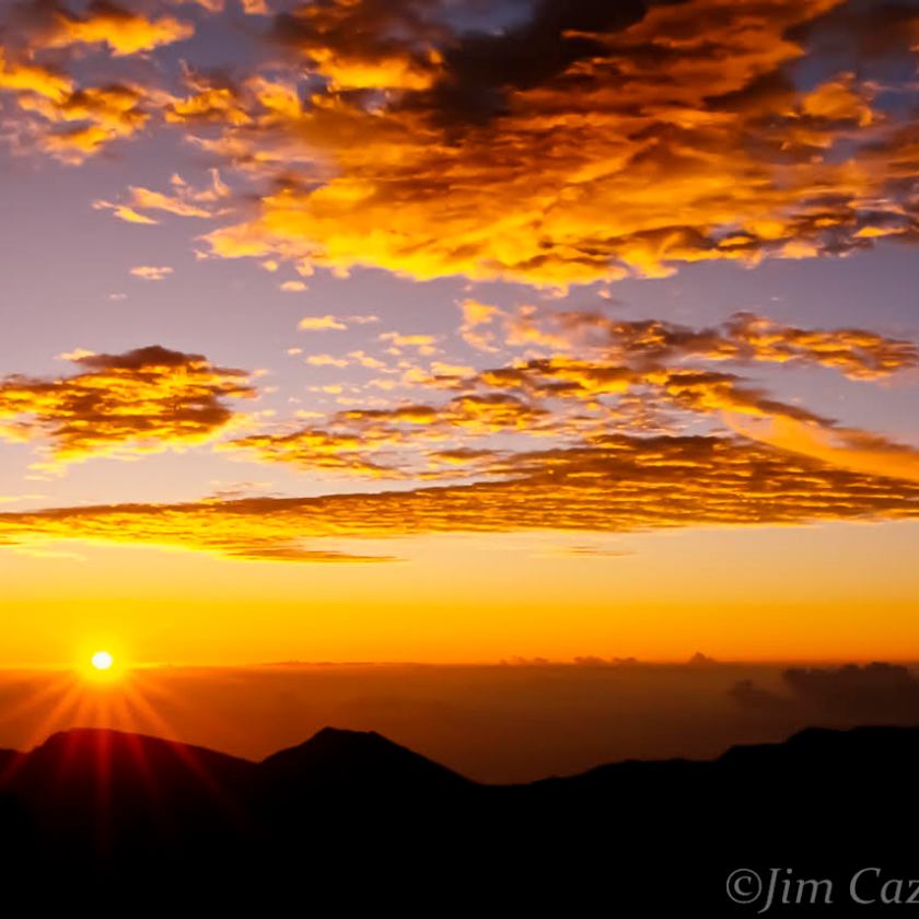 Sunrise over mountains with orange clouds and a silhouette of a rocky peak on the left.